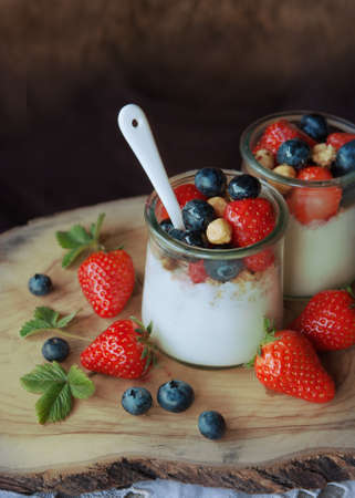 A glass of yogurt with blueberries and strawberries, granola and nuts on a wooden table, healthy breakfastの写真素材
