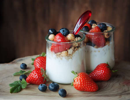 A glass of yogurt with blueberries and strawberries, granola and nuts on a wooden table, healthy breakfastの写真素材