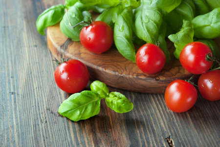 Bunch of fresh green basil and tomatoes, olive cutting board at rustic wooden backgroundの写真素材