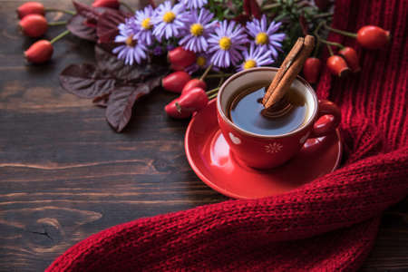Autumn background with cup of tea, flowers  and warm scarf on the wooden background. Autumn still life, spending autumn time at cozy homeの写真素材