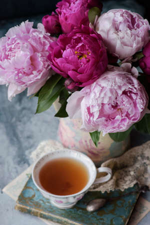 Beautiful flowers peonies in vase and cup of tea on the old book, vintage style decorの写真素材