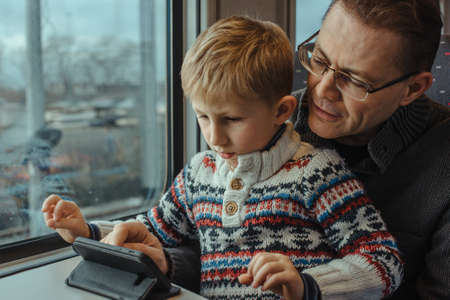 Father with his son traveling by train, together looking in smartphoneの写真素材