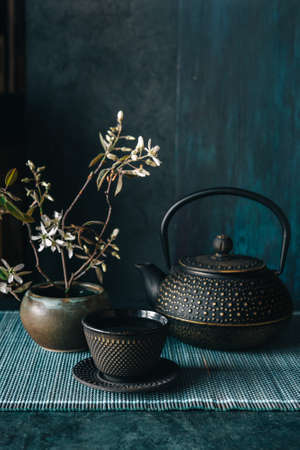 Black iron Asian teapot with cup of tea, wabi-sabi pot with spring flowerの写真素材