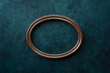 Vintage openwork wood golden oval frame on a old wall backgroundの写真素材
