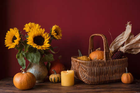 Thanksgiving table decor with pumpkins, sunflowers, corn in basket and candlesの写真素材