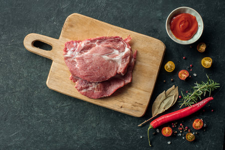 Raw pork meat with spices, hot pepper and tomato sauce for marinating on black background, Top view with place for textの写真素材