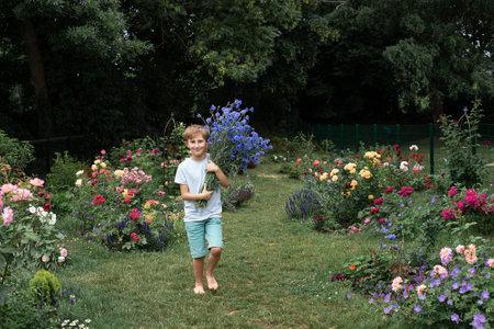 Boy holding a large bouquet of flowers cornflowers in a summer blooming rose gardenの写真素材
