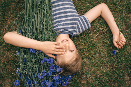 Happy blond boy lying on the grass with a bouquet of flowers cornflowersの写真素材