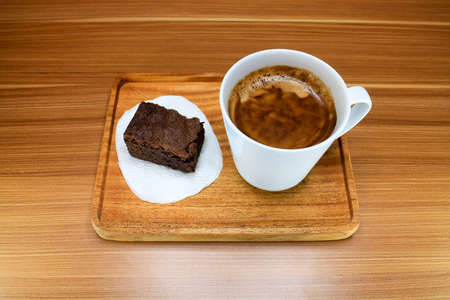 A cup of coffee with chocolate brownie cake served on a wooden tray.の写真素材