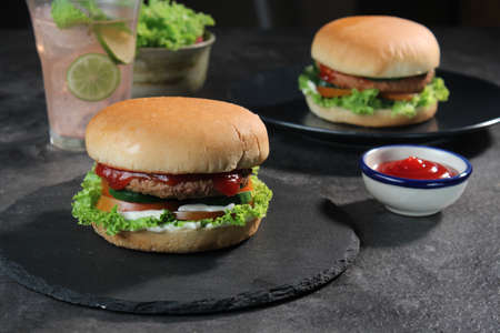 Two delicious fresh meat burgers with tomato sauce and vegetables on a dark background.の写真素材