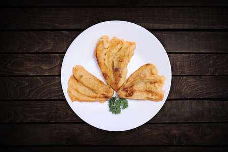 Three fried bananas on a top view white plate with a dark wood back screen.