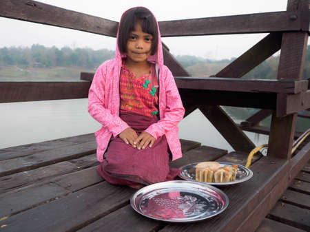Sangkhlaburi, Thailand- March 05, 2017: The unidentified Mon girl selling Tanaka, Burmese traditional facial powder, to tourist who are visiting the Mon bridge, the longest wooden bridge in Thailand.のeditorial素材