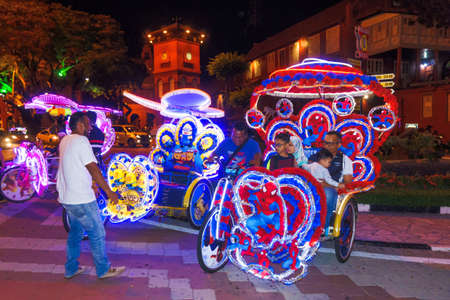 Melaka, Malaysia - April 20, 2017: Colourful trishaws decorated with bright multi-colour lights and cartoon pictures are ready to take passengers for sight-seeing the old town in night time.のeditorial素材