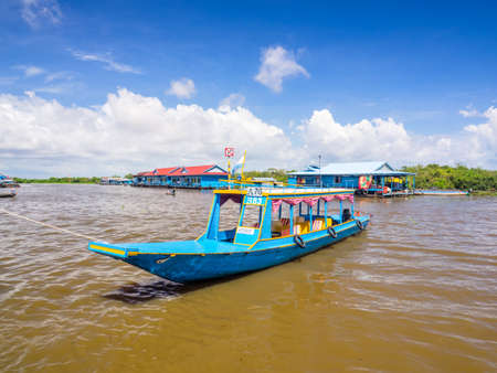 Siem Reap, Cambodia - October 29, 2016: A blue tourist boat docking at  the bank of Tonle Sap, the freshwater lake in Siem Reap, Cambodia, with a floating house and a floating school are at the background.のeditorial素材