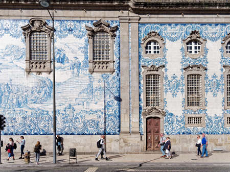 Porto, Portugal -  October 03, 2019: People walk on the footpath in front of the extraordinary side wall of the Carmo Church which  is decorated with ceramic tiles brightening with their specific white and blue art.のeditorial素材
