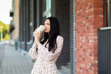 A young woman enjoys a coffee on the street on a summers day. Lifestyle in the city. A moment of relaxation. Coffee pause.の写真素材