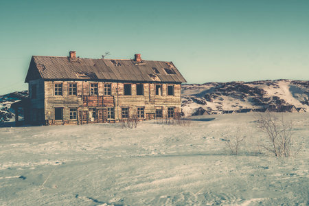 The old abandoned wooden building in a snow field of Russian Arctic during the cold winter at Teriberka, Murmansk region of Russia.の写真素材