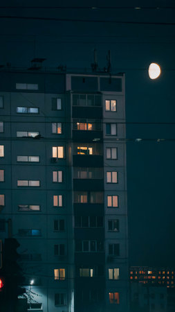 The night photo of multi-storey panel building, with light at the apartment buildings, and bright moon in the sky, at Novosibirsk, Russia.の写真素材