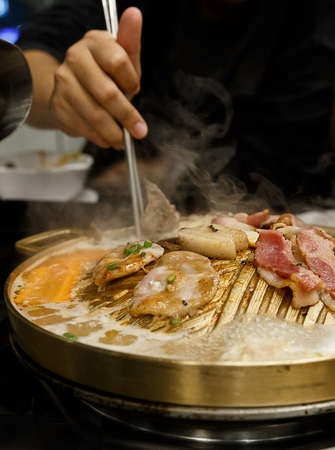 Use hand with stainless chopsticks picking up grilled roasted pork slice on korean barbecue brass...