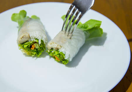 Noodle salad with mackerel wrapped in rice paper and fork on white plate.