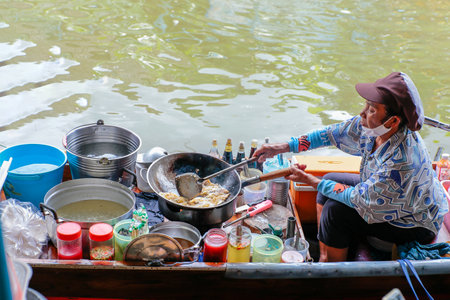 Nonthaburi, THAILAND - November 1, 2020: Old woman seller is cooking the omelet in the boat Wat Takhian Floating Market at Nonthaburi, very famous for tourist.のeditorial素材
