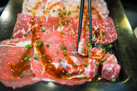 Chopsticks with Raw slice wagyu beef in black plastic tray, focus selective.の写真素材