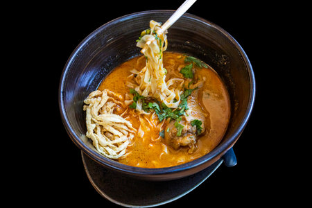 Northern Thai Khao Soi Chicken Curry Noodles in black bowl on black background.