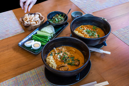 Curry noodles soup with beef and chicken in black bowl on wooden table background.