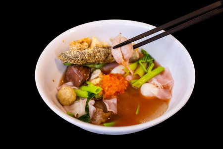 Die cut of Yentafo Pink seafood flat noodles with fish meatballs on black isolated.