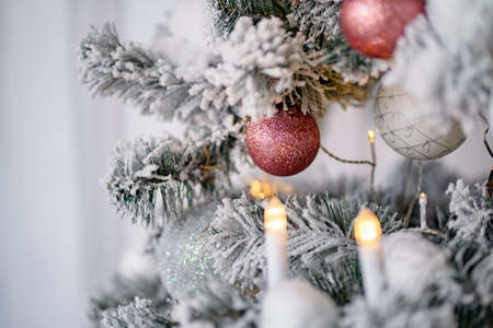 close-up of snowy christmas tree, decorated balls, garland, candles, snowballs