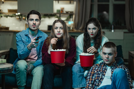 The youth company watches TV and eats popcorn with interest at a house partyの写真素材