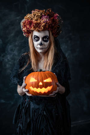 a woman in the image of a witch holds a Halloween pumpkin with a lanternの写真素材