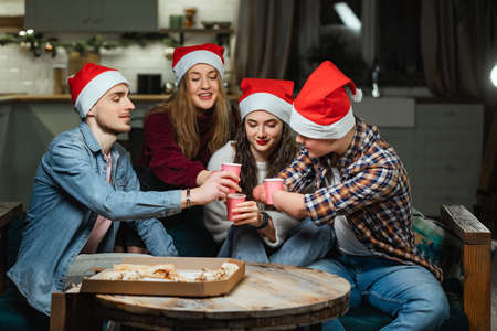company of men, women in santas red hats celebrate new year with pizzaの写真素材