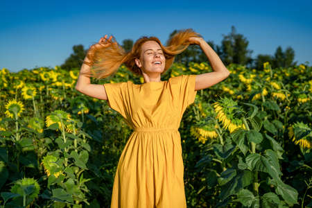 Portrait of happy smiling young caucasian red-haired woman in a sunflower fieldの写真素材