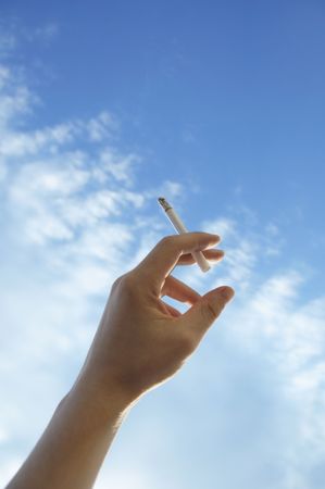 hand with a cigarette against the skyの写真素材