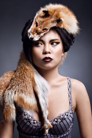 portrait of a beautiful girl with extravagant makeup and skin red fox on her headの写真素材