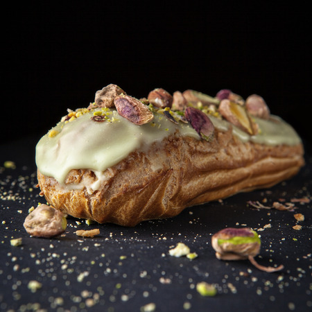 exquisite cream dessert eclair with pistachios with crumbs on the backgroundの写真素材