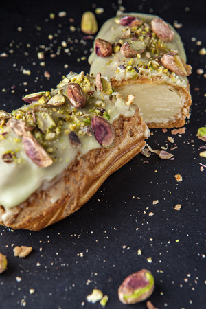 exquisite cream dessert eclair with pistachios with crumbs on the background