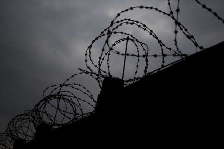 Fence with barbed wire in front of dark grey sky. Selective focus.の写真素材