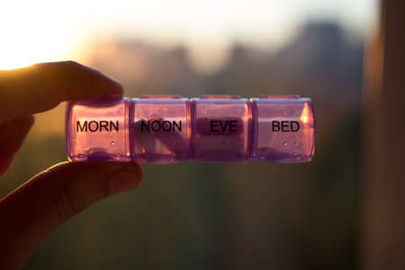 Close up view of man holding pill box in front of sunrise.
