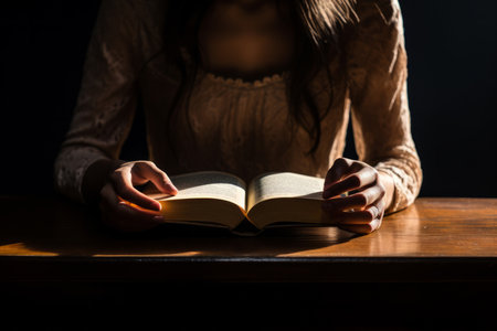 This beautifully composed image focuses on a woman's hand delicately holding an open book, bathed in soft natural light that casts long, graceful shadows. It captures the essence of tranquil reading momentsの素材