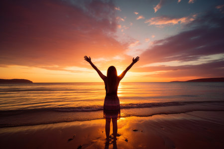 In this captivating image, a happy woman raises her arms in celebration, basking in the freedom and joy of a beautiful beach sunset. It captures the essence of wellness, success, freedom, and the spirit of travel. An inspiring visual for a wide range of conceptsの素材