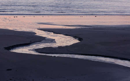 A stream of water naturally cut into the sand running into the oceanの写真素材