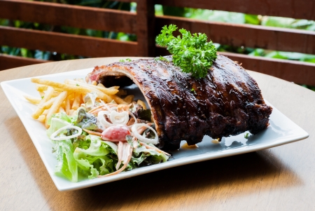 grilled juicy barbecue pork ribs in a white plate with fries,salad and parsley の写真素材