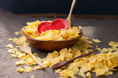 corn flakes in wooden bowl with spoons and Red heart on a table