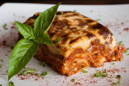 Lasagna on a square white plate with Italian basilの写真素材