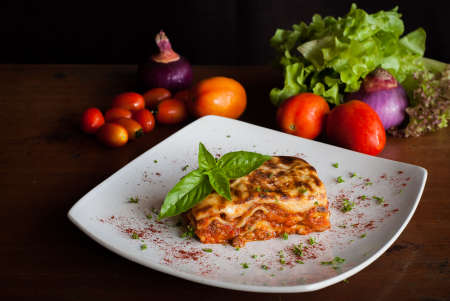 Lasagna on a square white plate with Italian basil
