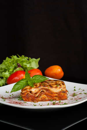Lasagna on a square white plate with Italian basil