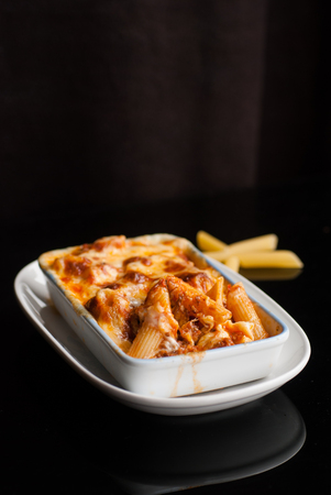 Baked penne pasta with tomato sauce and cheese in White bowlの写真素材
