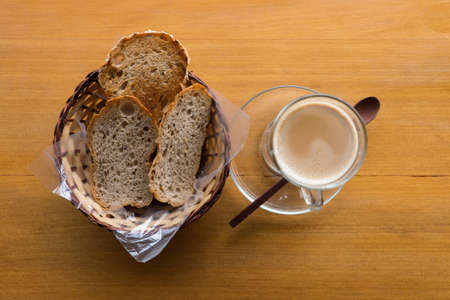 A cup of hot cappuccino and bread on wooden tableの写真素材